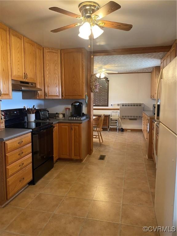 kitchen with under cabinet range hood, stainless steel microwave, freestanding refrigerator, black / electric stove, and light tile patterned floors