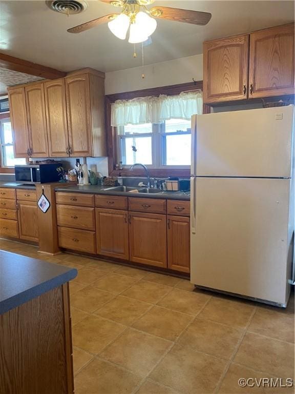 kitchen featuring dark countertops, stainless steel microwave, visible vents, freestanding refrigerator, and a sink