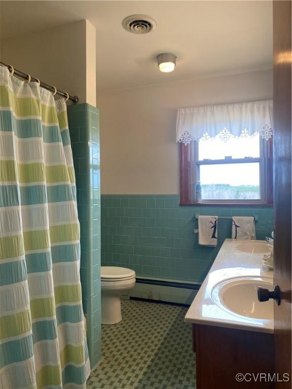 full bathroom featuring visible vents, toilet, a sink, tile walls, and baseboard heating