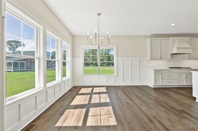 unfurnished dining area featuring visible vents, dark wood-type flooring, recessed lighting, an inviting chandelier, and a decorative wall