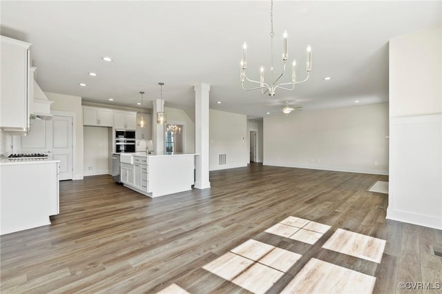 unfurnished living room featuring visible vents, baseboards, recessed lighting, light wood-style floors, and ceiling fan with notable chandelier