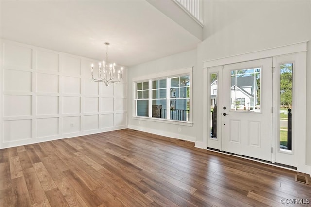 foyer entrance featuring visible vents, an inviting chandelier, hardwood / wood-style floors, and a decorative wall