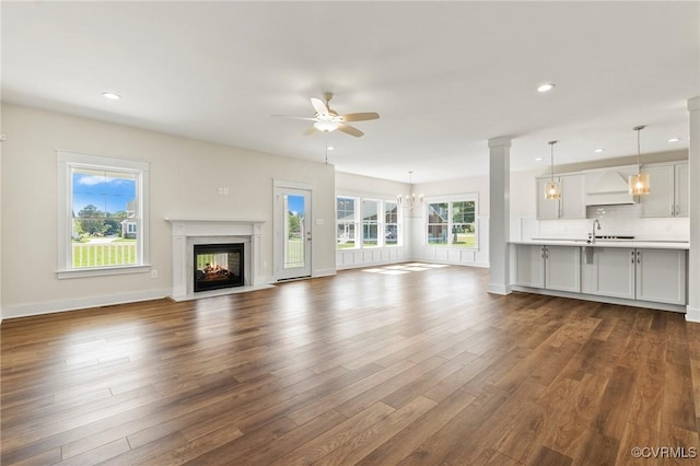 unfurnished living room with dark wood-type flooring, a premium fireplace, recessed lighting, ceiling fan with notable chandelier, and a sink