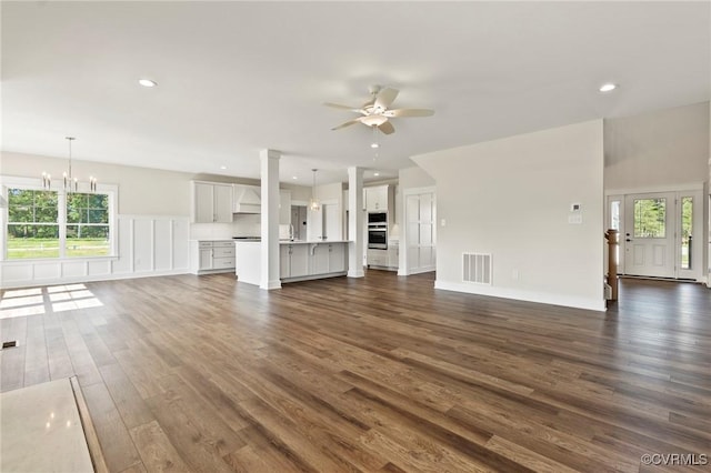 unfurnished living room with a wealth of natural light, visible vents, ceiling fan with notable chandelier, and dark wood-style flooring