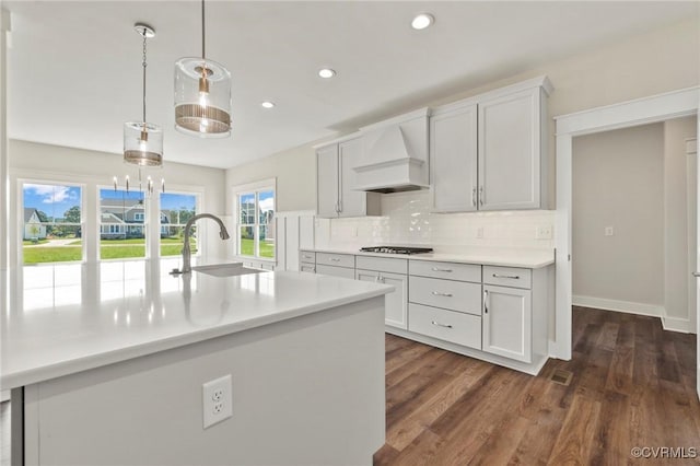 kitchen featuring tasteful backsplash, premium range hood, light countertops, dark wood-style floors, and gas stovetop