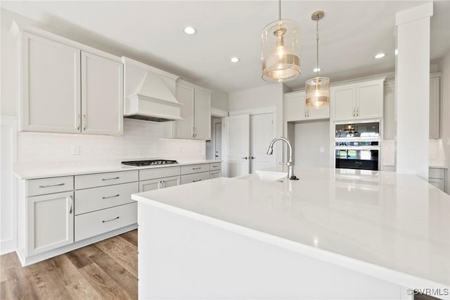 kitchen featuring premium range hood, light countertops, stainless steel oven, gas stovetop, and a sink