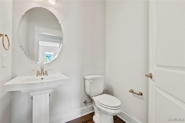 half bath with a sink, baseboards, toilet, and wood finished floors