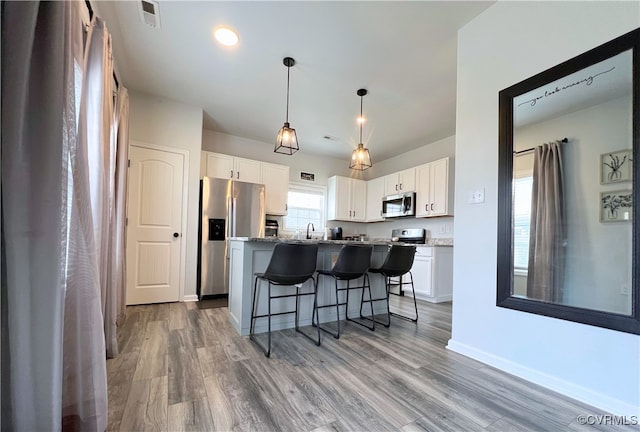 kitchen with a breakfast bar area, wood finished floors, white cabinets, stainless steel appliances, and a sink