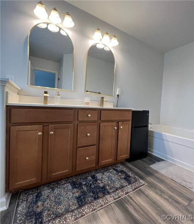 bathroom featuring double vanity, a sink, a bath, and wood finished floors