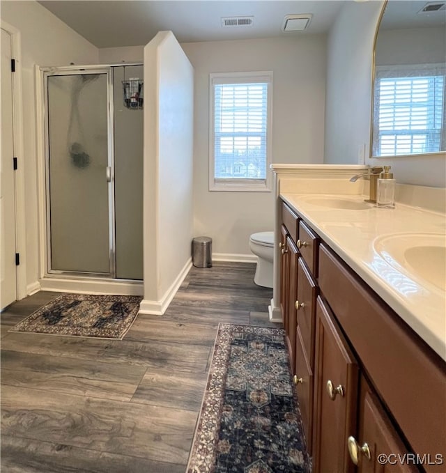 full bath with visible vents, double vanity, a stall shower, wood finished floors, and a sink