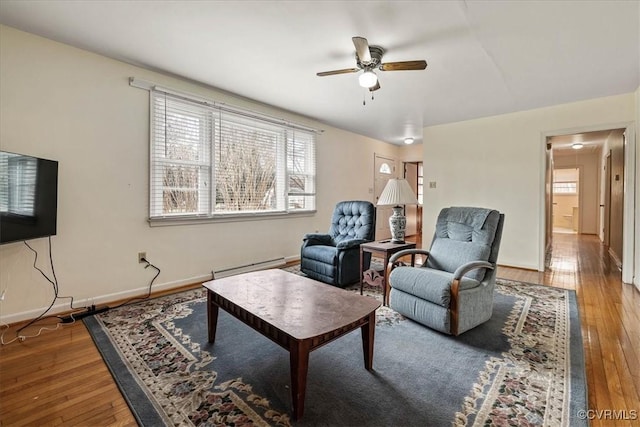 living room featuring baseboard heating, ceiling fan, baseboards, and wood-type flooring