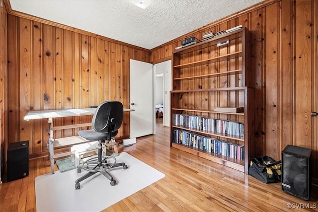 office area with wood walls, a textured ceiling, ornamental molding, and wood finished floors