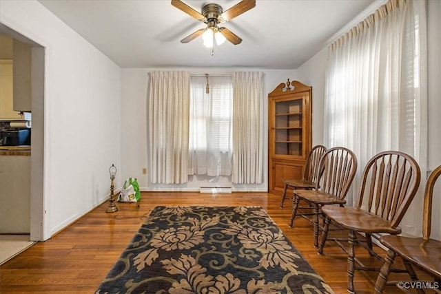 living area featuring ceiling fan, baseboard heating, and wood finished floors