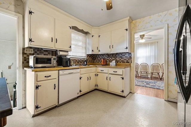 kitchen featuring wallpapered walls, dishwasher, cream cabinetry, refrigerator, and a sink