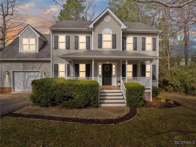 colonial-style house featuring driveway, roof with shingles, a porch, a yard, and a garage