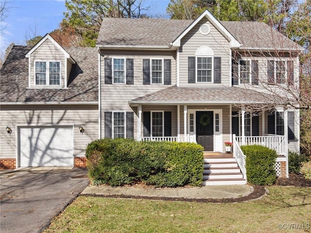 colonial inspired home featuring a garage, aphalt driveway, covered porch, and a shingled roof