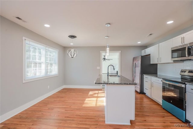 kitchen featuring tasteful backsplash, dark stone counters, light wood-type flooring, appliances with stainless steel finishes, and a sink