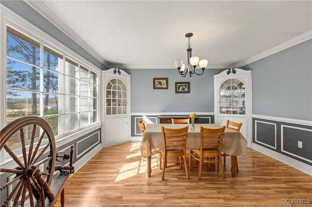 dining room featuring crown molding, a chandelier, light wood-style flooring, wainscoting, and a decorative wall