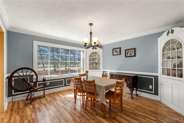 dining area featuring a chandelier, wood finished floors, ornamental molding, and wainscoting