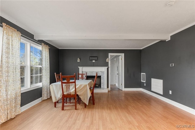 dining space with beamed ceiling, light wood-style floors, baseboards, and a high end fireplace