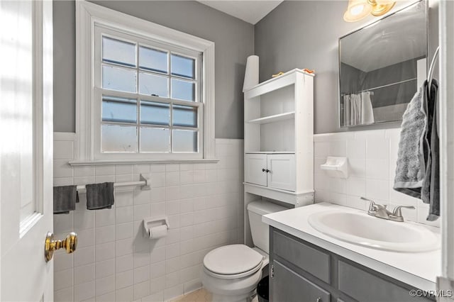 full bathroom with a wainscoted wall, toilet, tile walls, and vanity