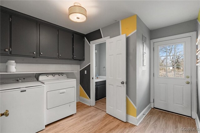 laundry area featuring baseboards, cabinet space, a sink, washer and dryer, and light wood-type flooring