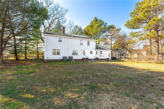 back of house with solar panels, fence, a lawn, cooling unit, and a chimney