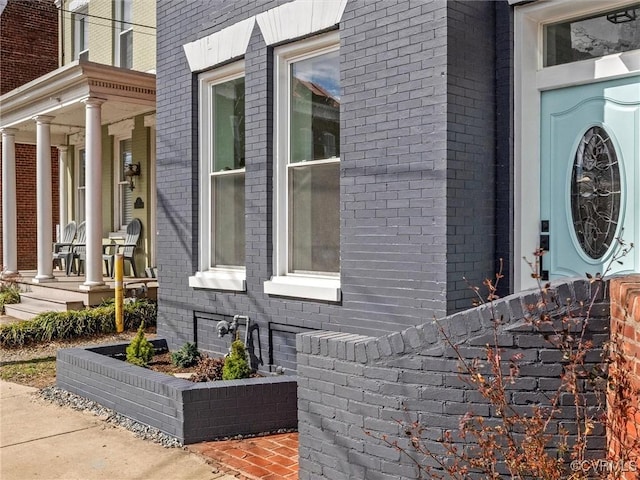 doorway to property featuring brick siding and a porch