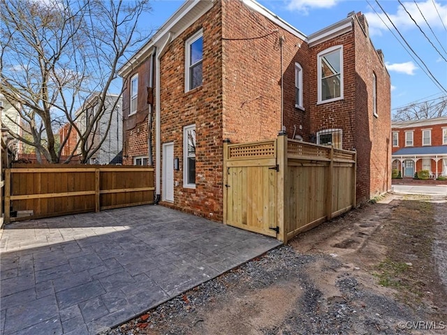 view of side of property featuring brick siding, a patio area, a gate, and fence