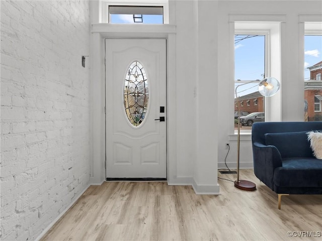 foyer entrance featuring light wood-style floors, baseboards, and brick wall