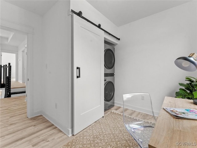 washroom with wood finished floors, baseboards, laundry area, a barn door, and stacked washer / dryer