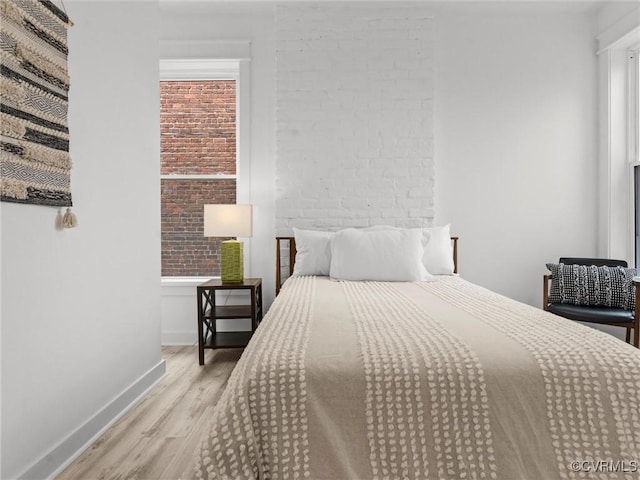 bedroom featuring baseboards, wood finished floors, and brick wall