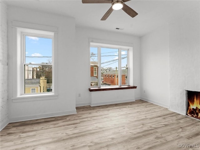 empty room featuring visible vents, a fireplace, light wood-type flooring, and baseboards