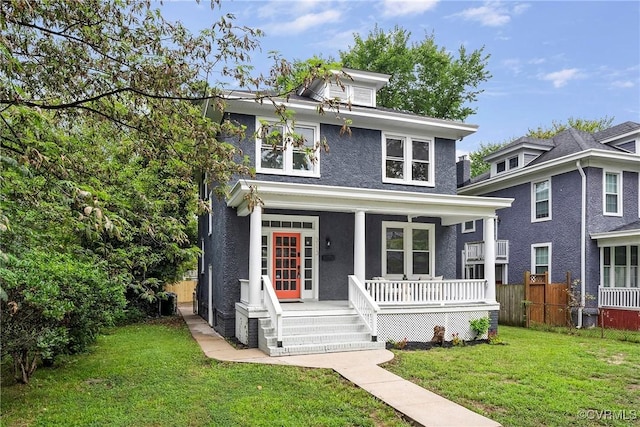 american foursquare style home with stucco siding, covered porch, a front yard, and fence