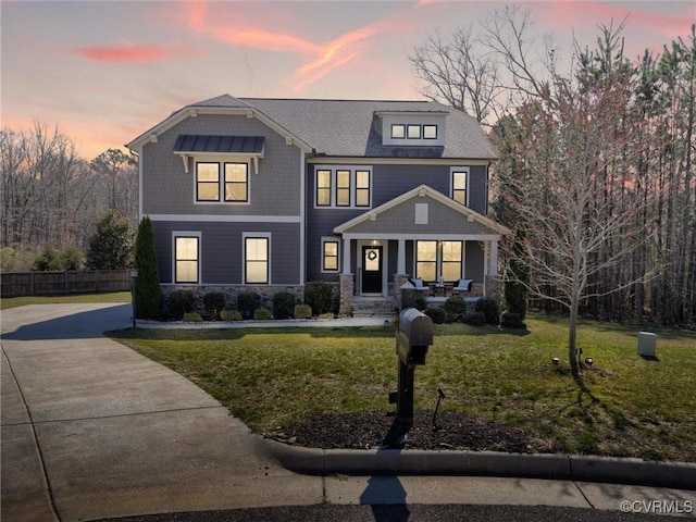 view of front facade featuring a porch, fence, a lawn, and stone siding