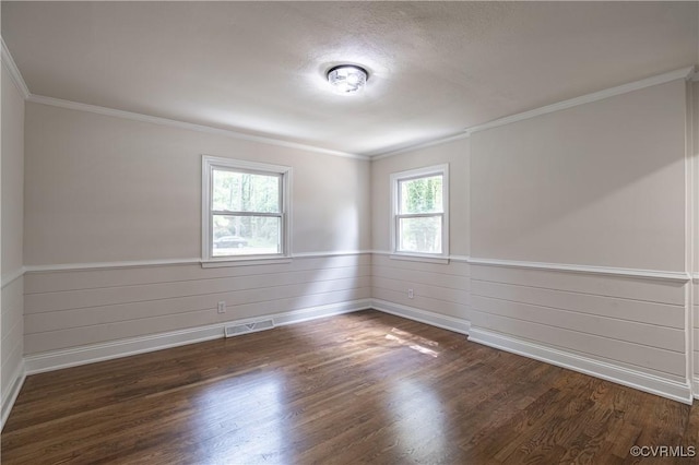 spare room featuring crown molding, dark wood-style floors, visible vents, and wainscoting