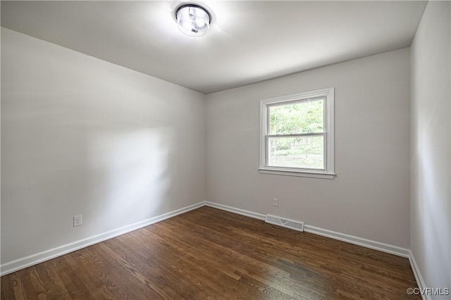 unfurnished room with dark wood-style floors, visible vents, and baseboards