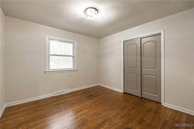 unfurnished bedroom featuring visible vents, baseboards, dark wood-type flooring, and a closet