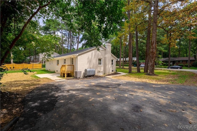 view of property exterior featuring brick siding, fence, central AC, a chimney, and heating fuel