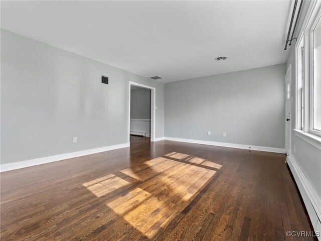 spare room with dark wood-style floors, visible vents, a baseboard heating unit, and baseboards