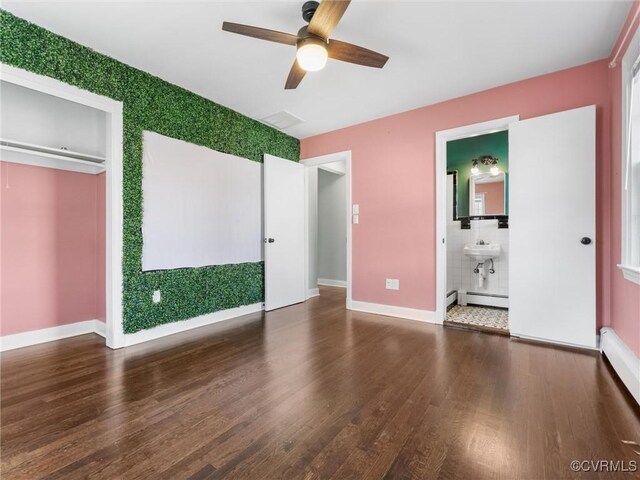 unfurnished bedroom featuring a sink, a baseboard heating unit, baseboards, and wood finished floors