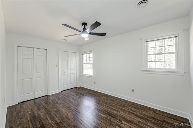 unfurnished bedroom with visible vents, two closets, a ceiling fan, dark wood finished floors, and baseboards