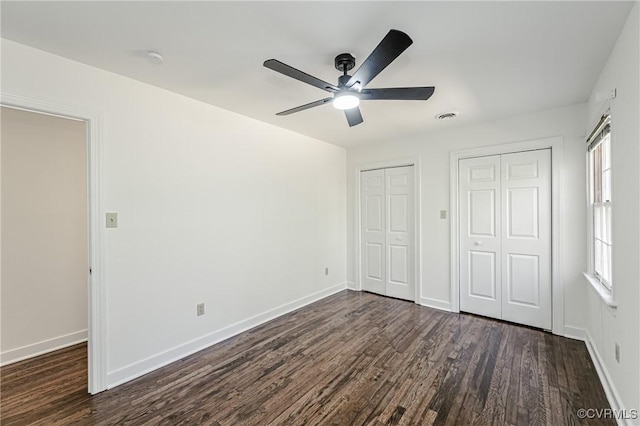 unfurnished bedroom featuring visible vents, baseboards, two closets, and dark wood finished floors