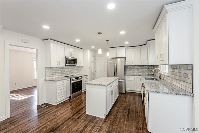 kitchen with a kitchen island, dark wood finished floors, stainless steel appliances, white cabinetry, and a sink