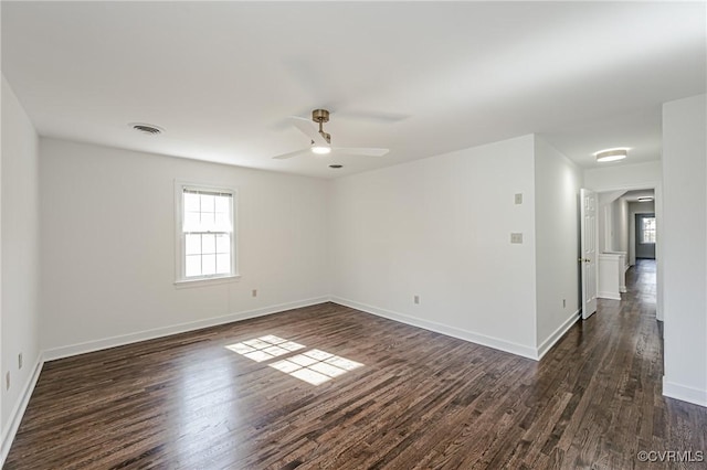 spare room featuring dark wood-style floors, visible vents, a ceiling fan, and baseboards