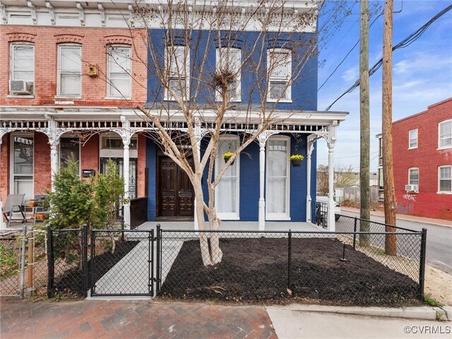 view of front of house with a gate, a fenced front yard, a porch, cooling unit, and brick siding