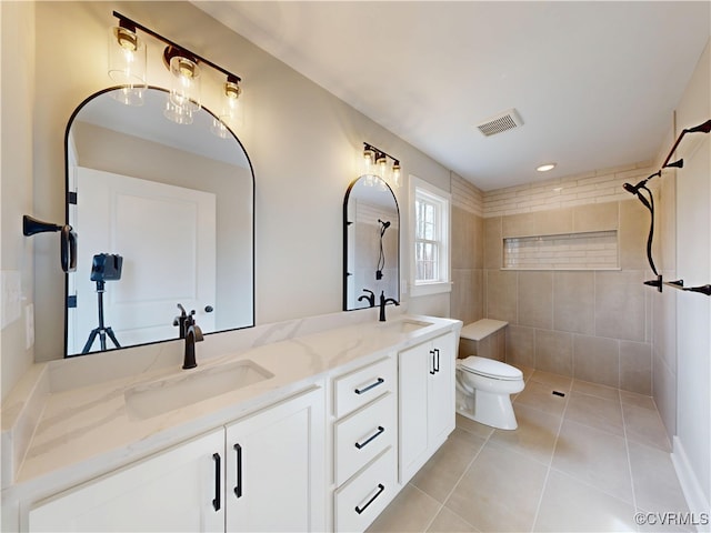 full bath featuring toilet, visible vents, a tile shower, and a sink