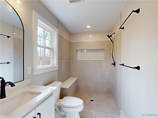 bathroom with visible vents, toilet, a tile shower, tile patterned floors, and vanity