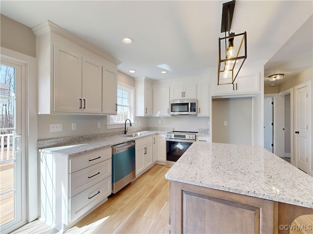 kitchen featuring light stone counters, light wood finished floors, a sink, stainless steel appliances, and a center island