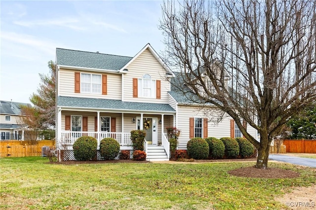 traditional-style home with roof with shingles, covered porch, a front yard, and fence